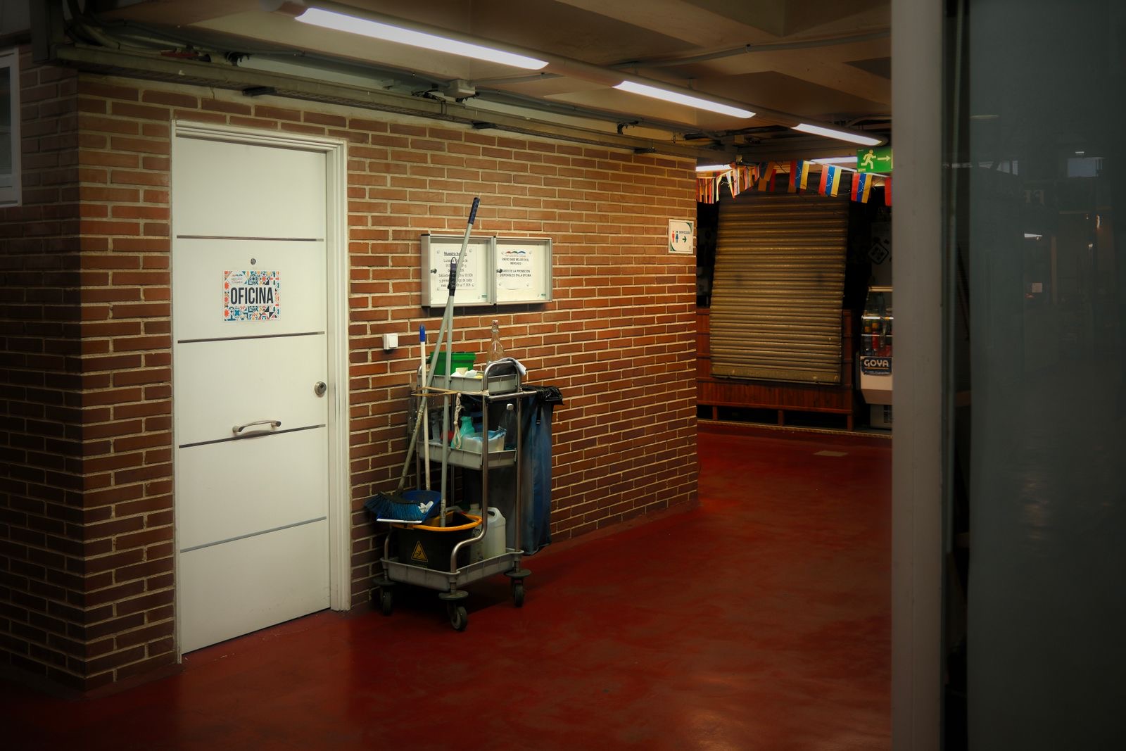 A cleaning trolley parked in a brick-walled service corridor under strip lights