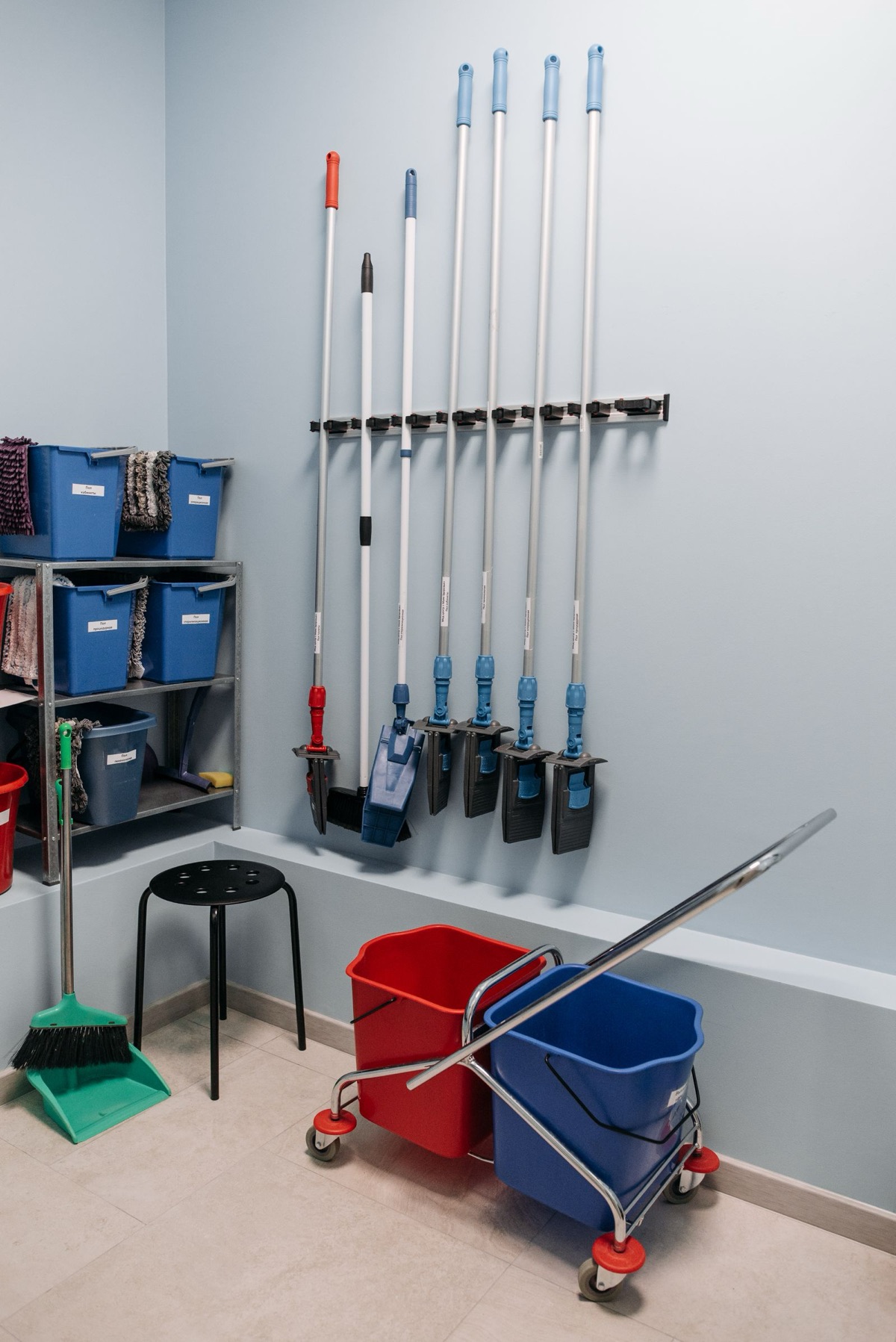 A cleaning store with mops and brushes hung on the wall, buckets and labelled bins on shelves